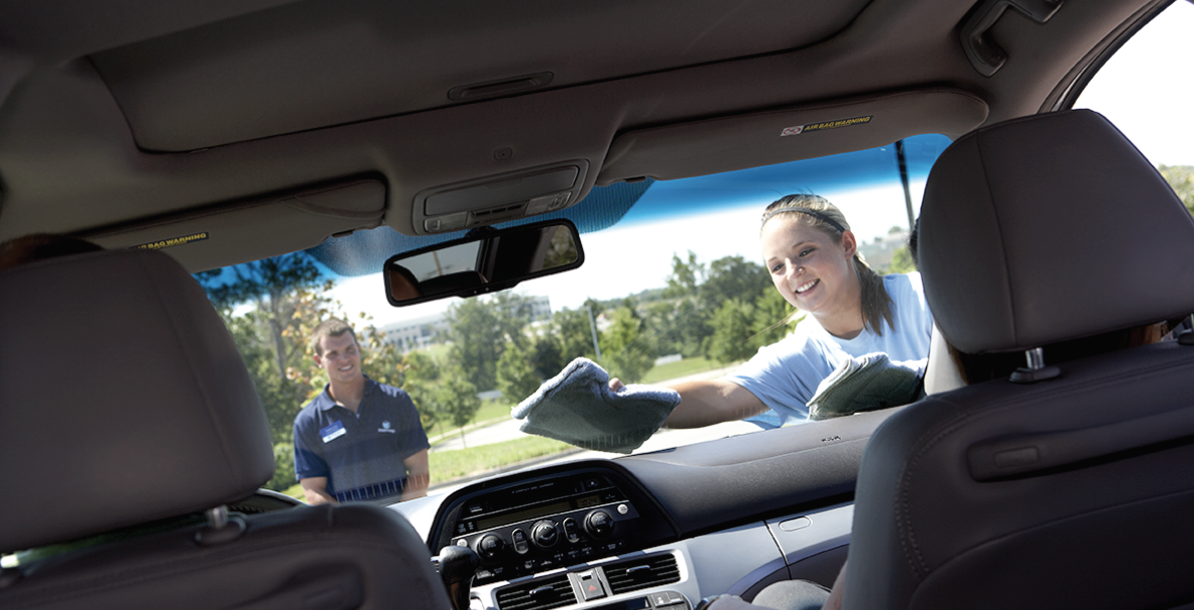 a woman is cleaning the dashboard of a car while a man looks on